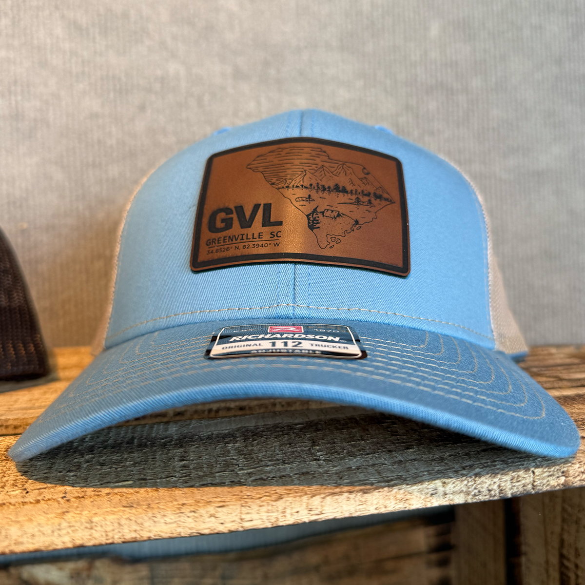 Blue cap with a leather patch featuring 'GVL' and a map on a wooden surface.