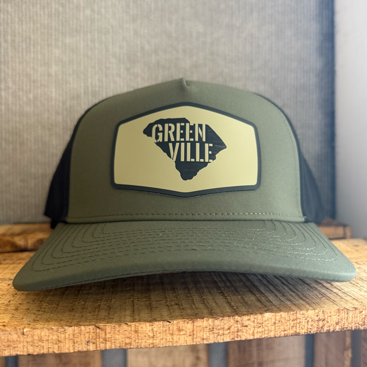 Green and black cap with 'Greenville' over a South Carolina state shape on wood surface.